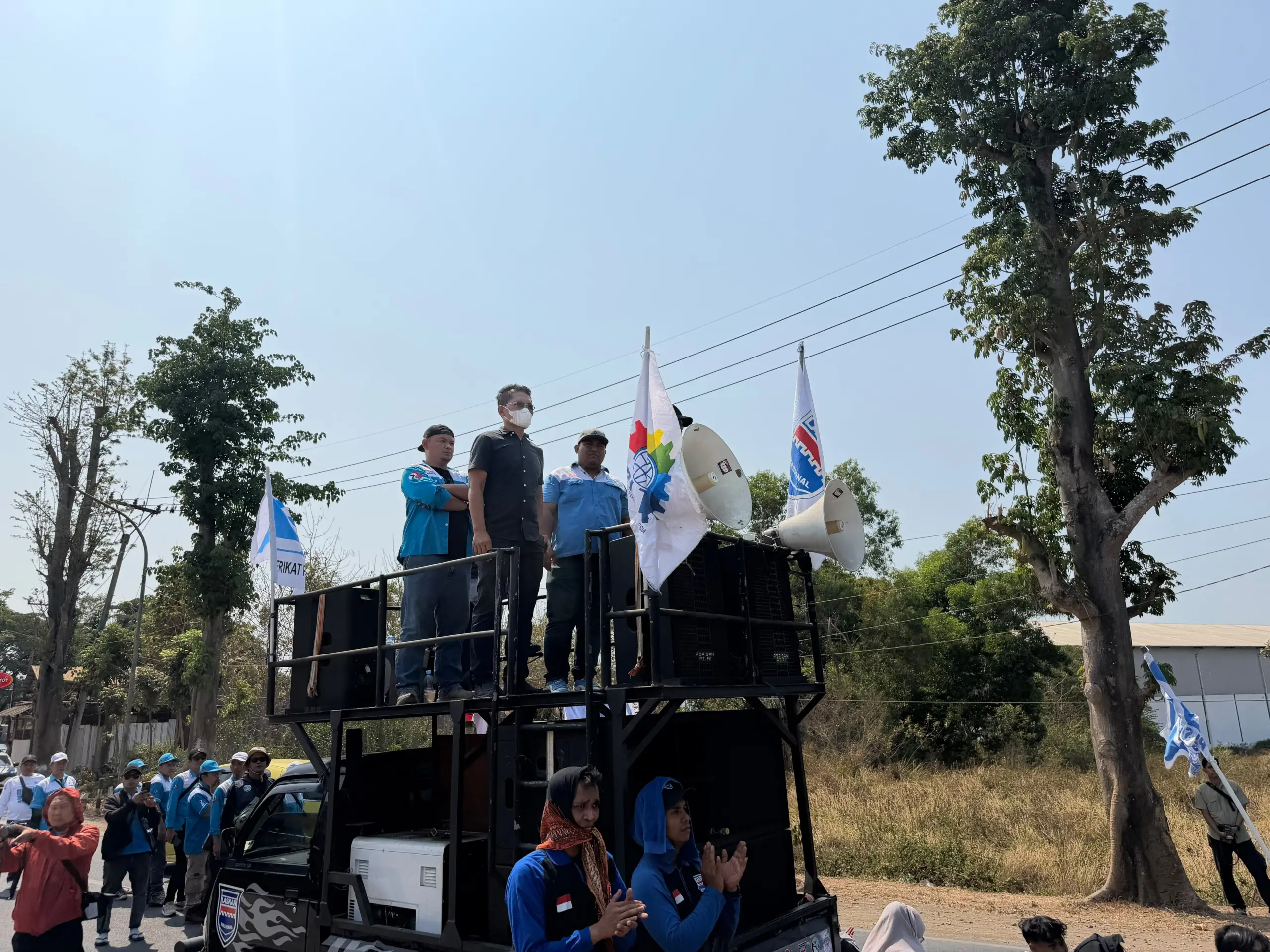 Tiga pengurus SPN berdiri di atas mobil komando dengan pengeras suara dan bendera